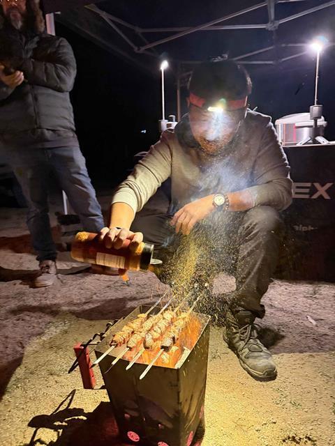 An AlphaRex employee cooking skewers over an open fire at the OVR Outpost during the 2026 King of the Hammers.